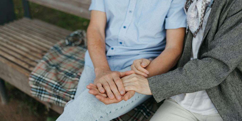 Kuvituskuva. Vanhempi pariskunta istuu vierekkäin ja pitelee toisiaan käsistä kiinni.